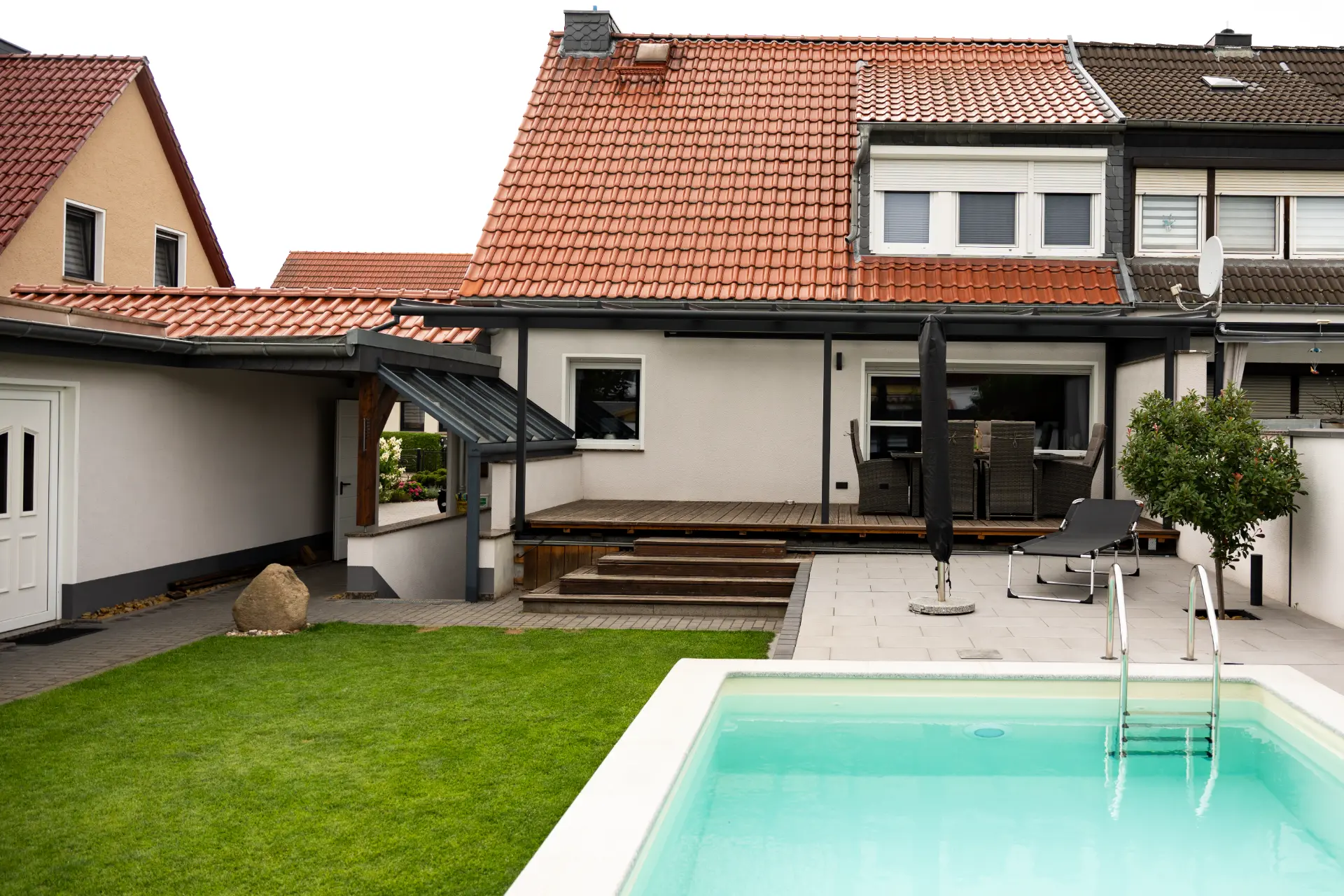 Terrassendach über einer Holzterrasse mit Stufen an einem Reihenhaus, Pool im Vordergrund